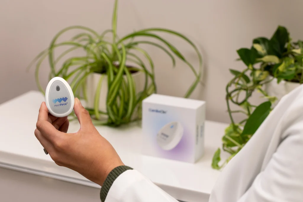 Eine Hand hält den CardioClin-Sensor; im Hintergrund ist die Produktverpackung zu sehen.